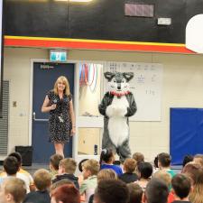 Principal standing with Husky Mascot at school assembly. 