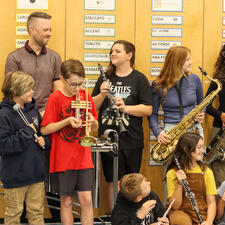 Group of students holding new instruments. Adult looks on at them.